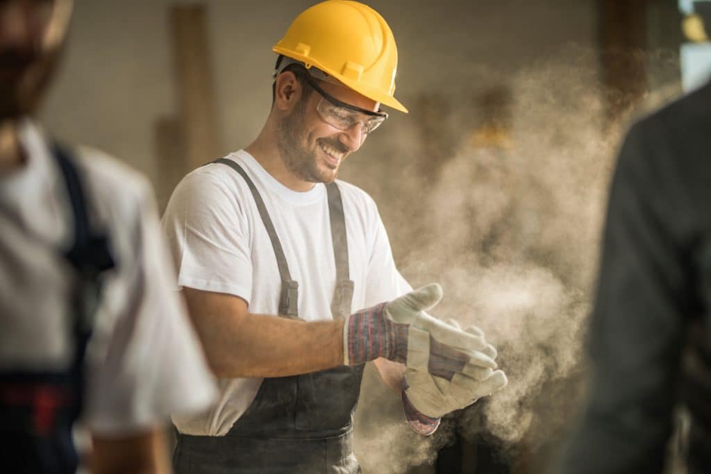 Happy manual worker cleaning his gloves from sawdust at construction site.