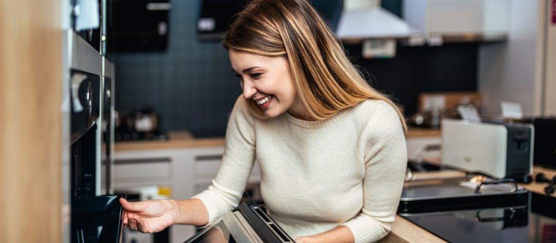 Young adult woman buying electric oven in tech in store.