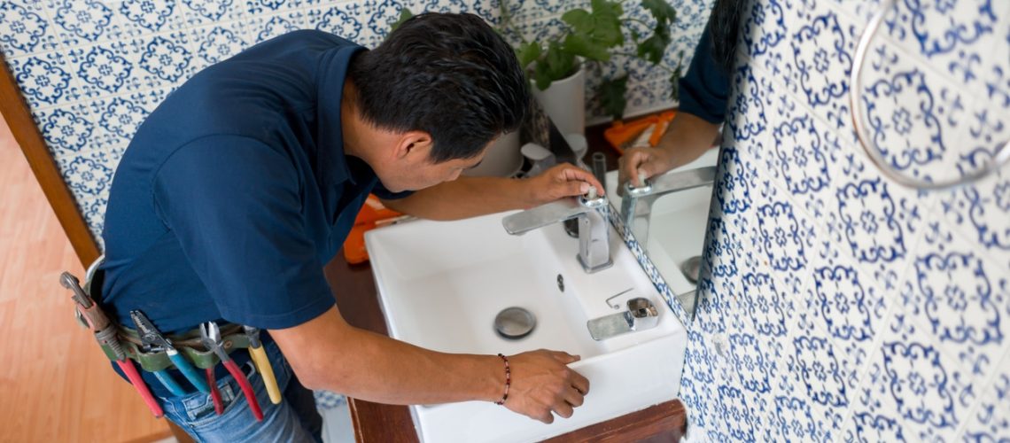 Latin American plumber installing a faucet in a bathroom's sink - home repairment concepts
