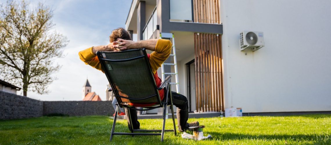Tired man relaxing on comfortable chair by paint equipment in yard outside apartment during sunny day